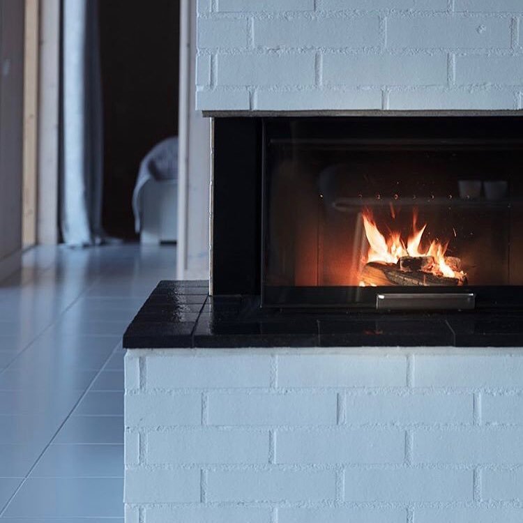 A modern, painted white brick fireplace with a sleek black tile hearth and a large black glass firebox insert, set low to the floor.