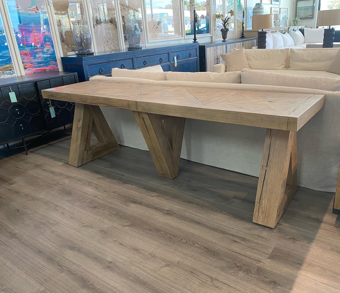 Large light wood console table with triangular legs behind a beige sofa