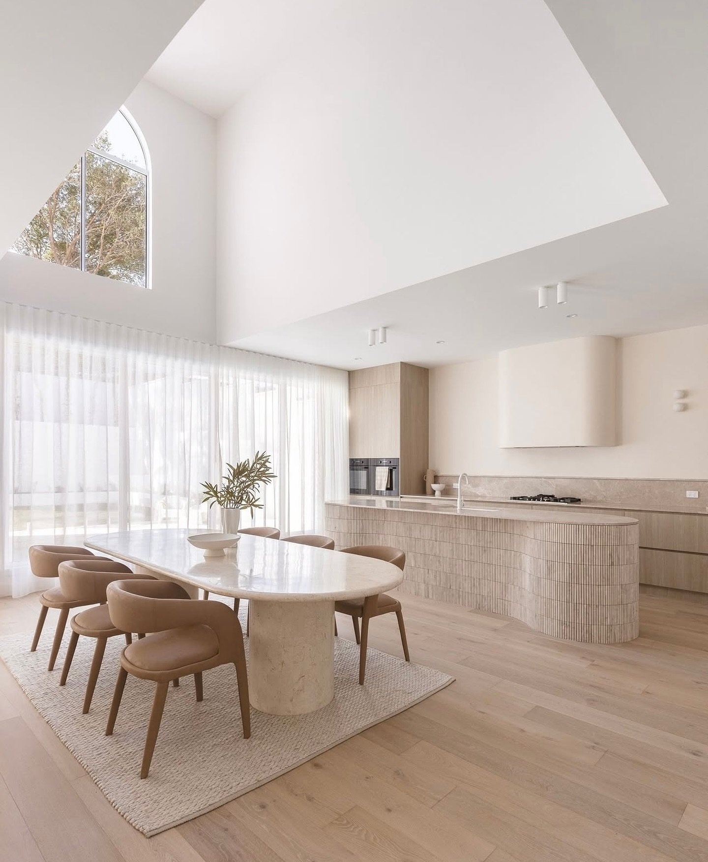 Oval cream stone dining table with tan leather chairs in high ceiling open plan room