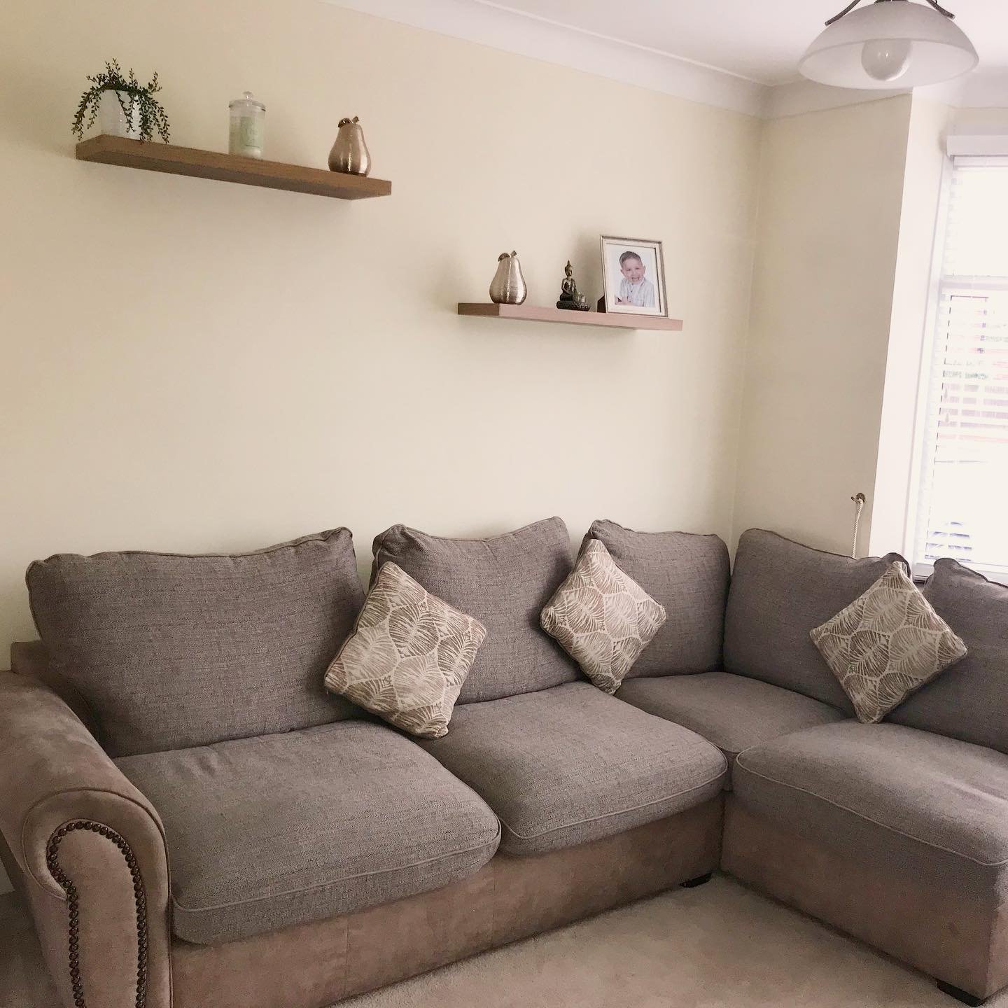 Staggered wooden floating shelves with minimal decor above a beige sectional sofa
