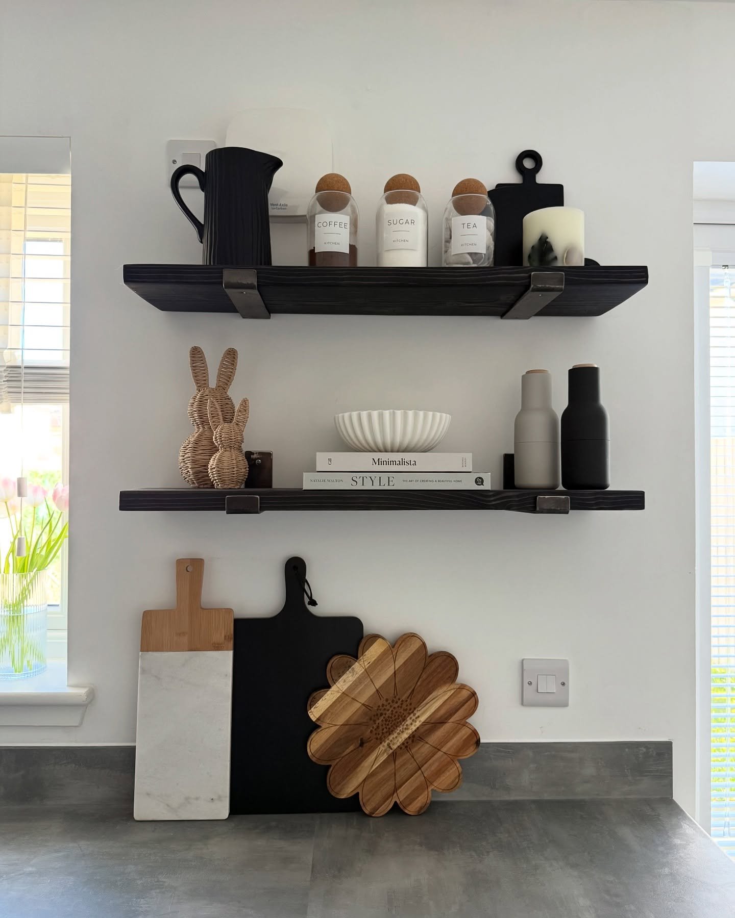 Two black floating shelves with metal straps, styled with white canisters and modern farmhouse decor.