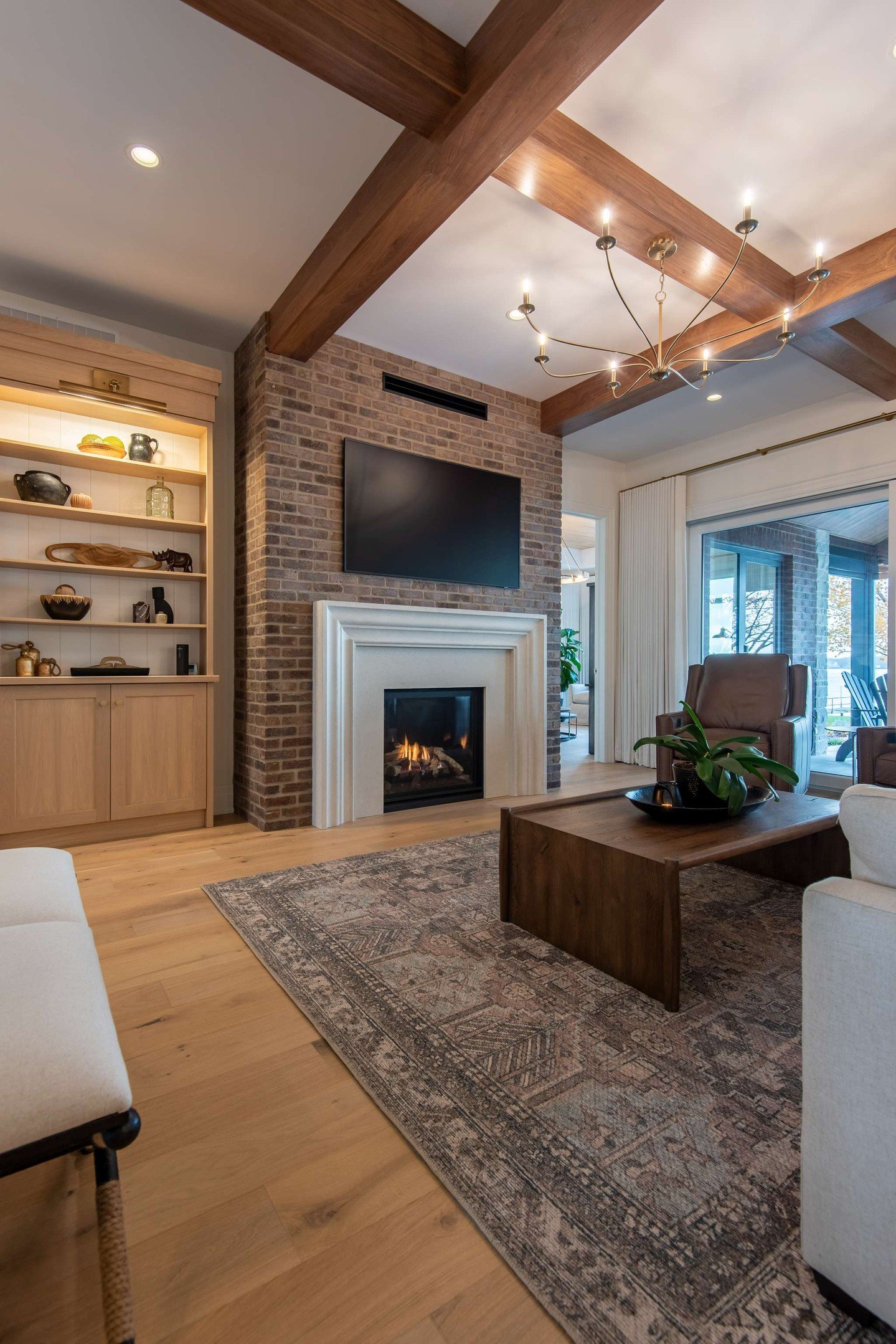 A living room fireplace with a floor-to-ceiling rustic brick chimney breast. A white wooden mantel frames the firebox, and a TV is mounted above it.