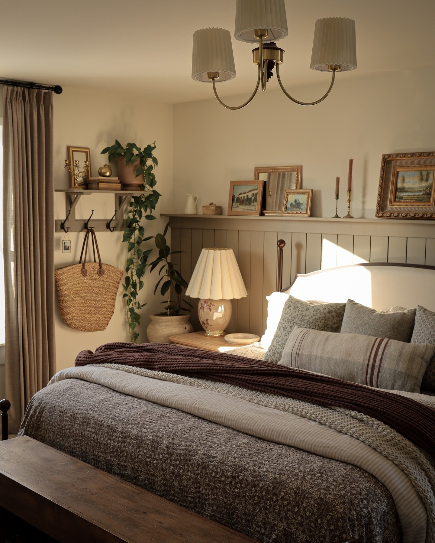 Cozy bedroom featuring beadboard wainscoting, a shelf with vintage art, floral bedding, and a pleated brass chandelier