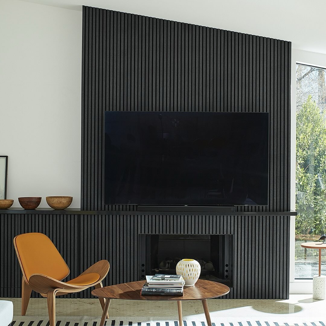 Modern living room with a fireplace and television mounted on a matte black vertical slatted accent wall with an asymmetrical mantel.