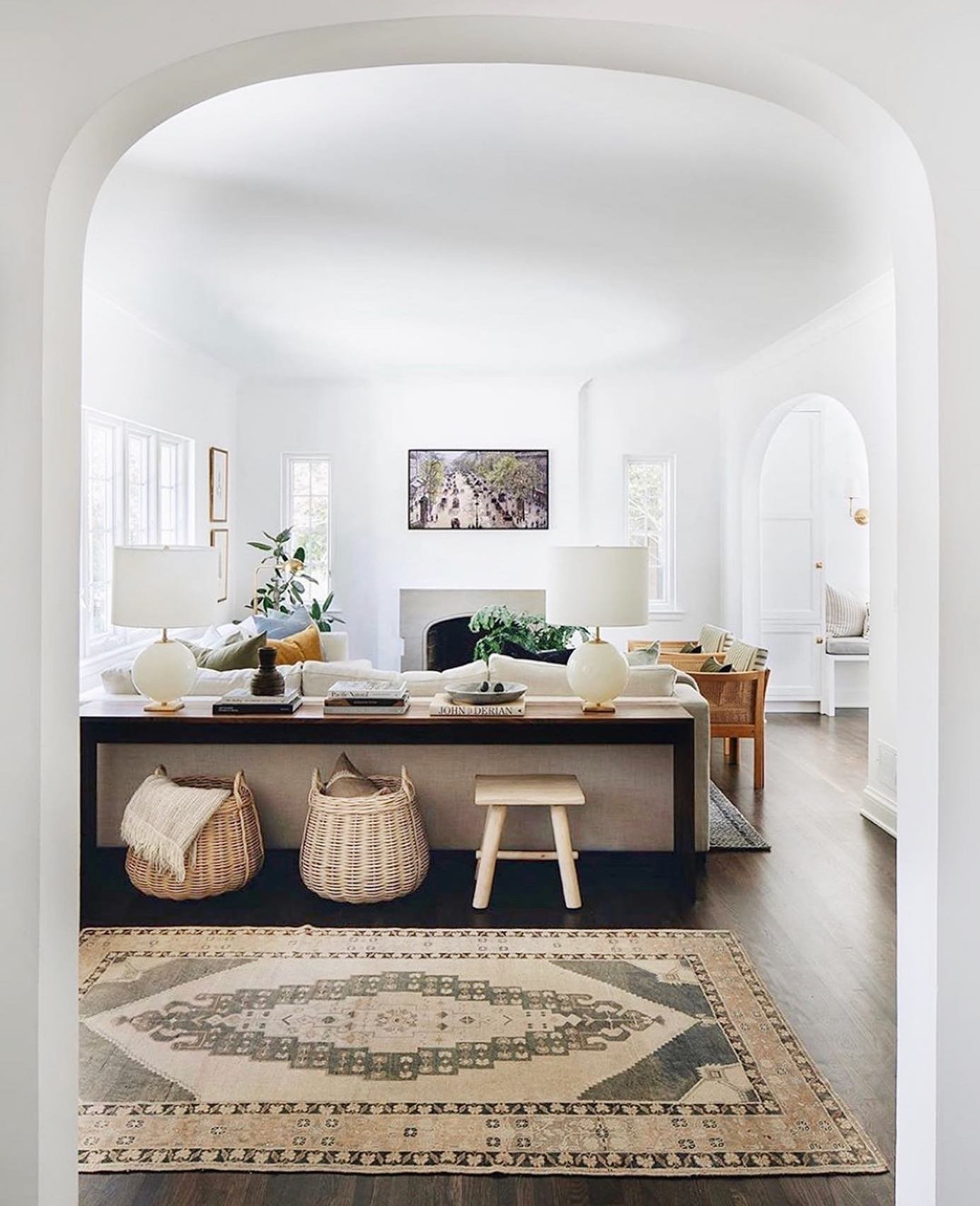 Long dark wood console table styled with white lamps and baskets behind a sofa