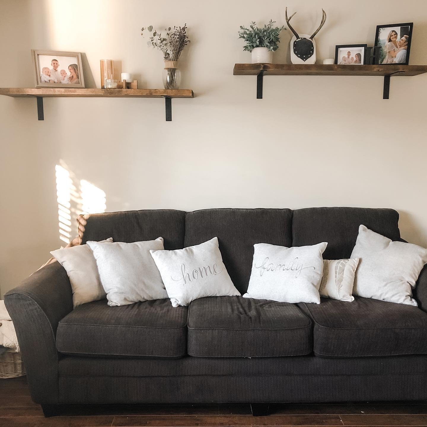 Two wooden shelves with black brackets displaying family photos and rustic decor above a dark grey sofa