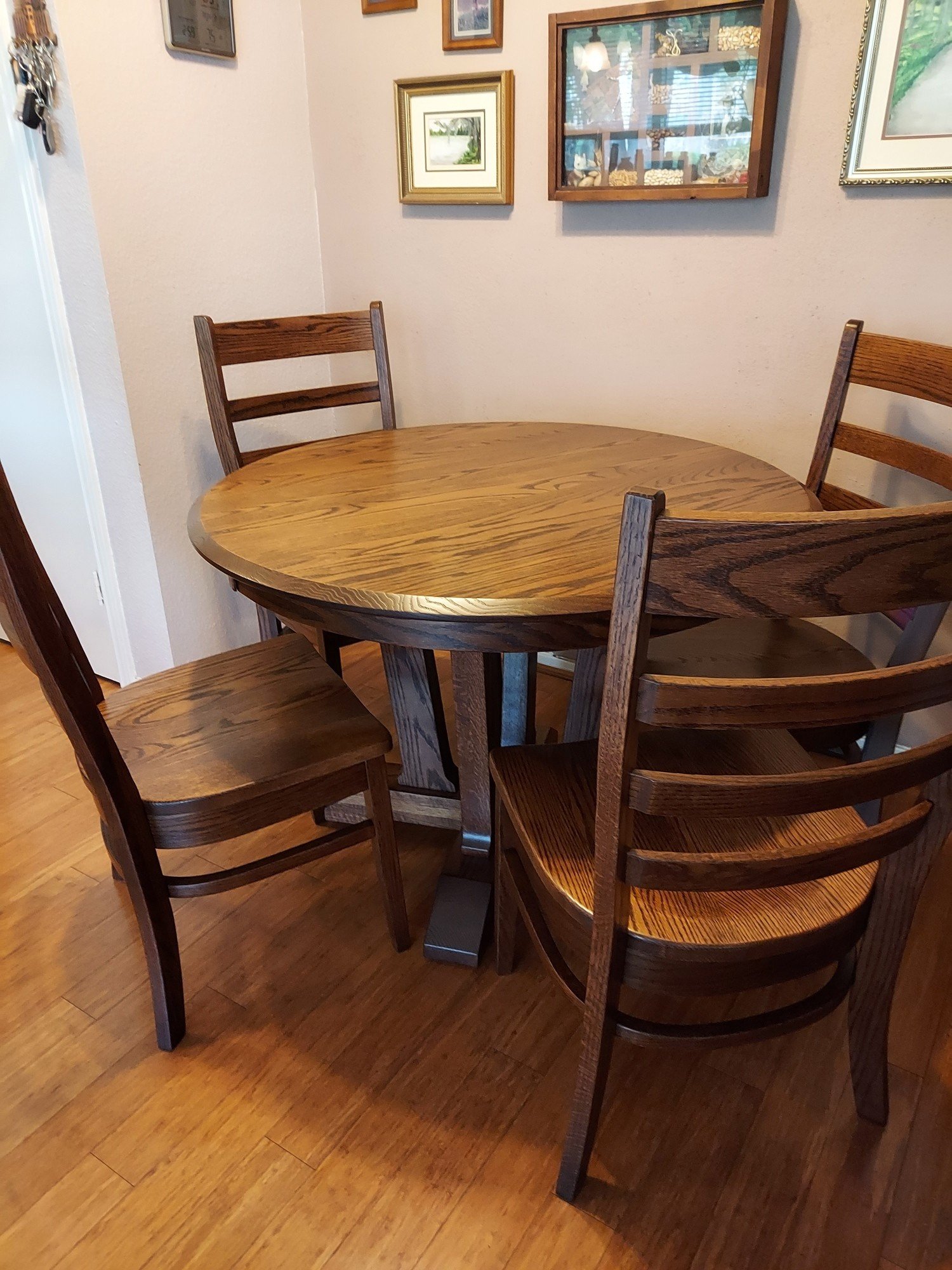 Round oak wood dining table with matching ladder back chairs on wood floor