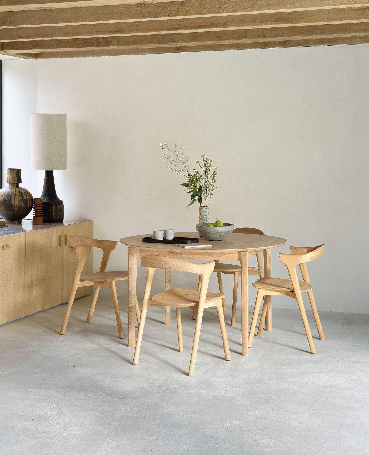 Round light oak dining table with matching wooden chairs under wood beams