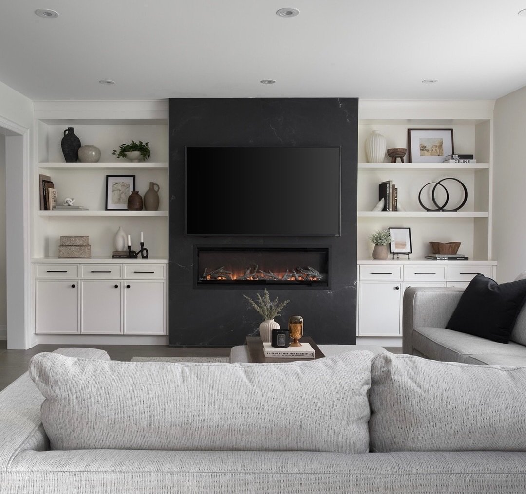 White built-in shelves with black hardware flanking a black marble fireplace wall