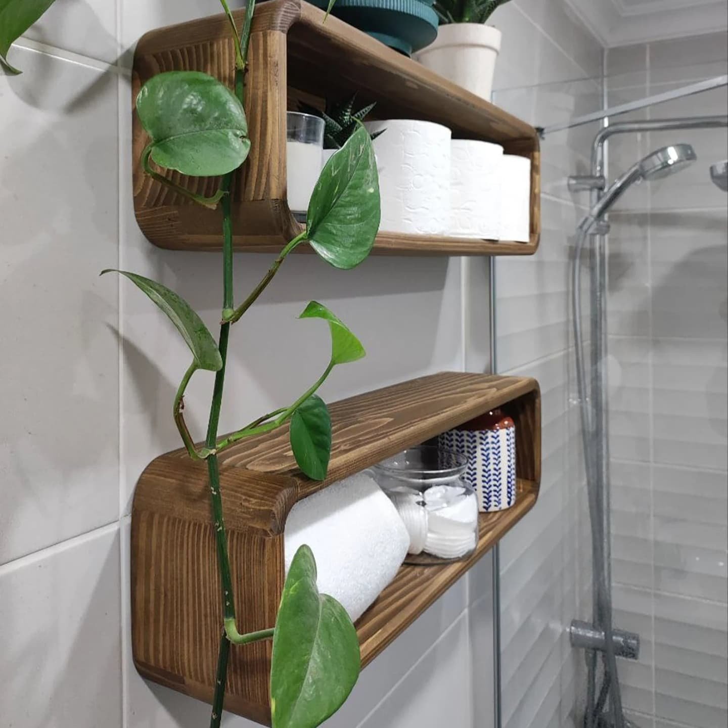 Two dark wood floating box shelves with rounded corners, mounted on a tiled bathroom wall, holding toilet paper and towels.