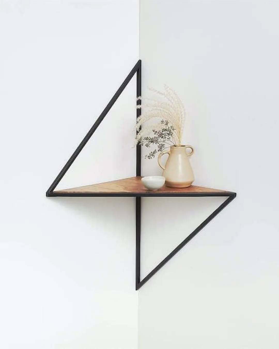 Diamond-shaped black metal wire frame holding a wooden triangular shelf in a white corner.