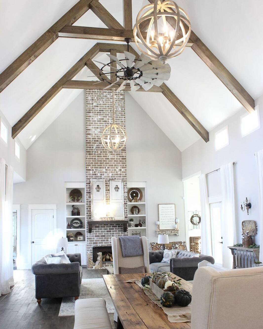 A grand, floor-to-ceiling brick fireplace with a whitewash finish, extending into a high vaulted ceiling. It is flanked by built-in shelves and features a hanging orb chandelier.