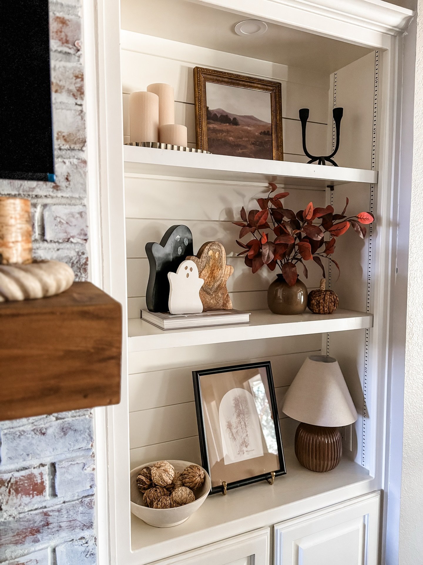 White built-in shelves with shiplap backing featuring Halloween ghosts and autumn decor next to a brick fireplace.