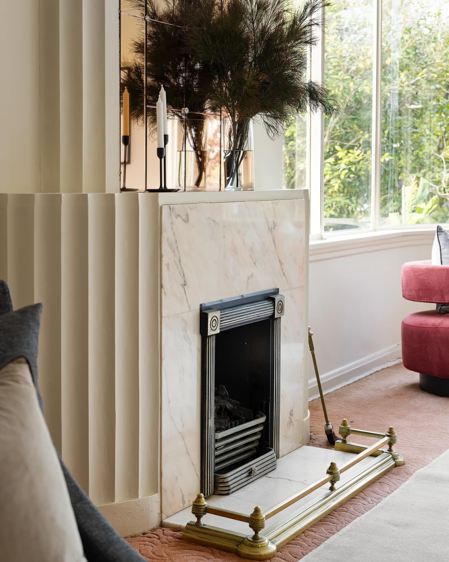 An Art Deco-inspired fireplace featuring a pink-veined white marble surround, an original black metal firebox, and a dramatic fluted plaster chimney breast.