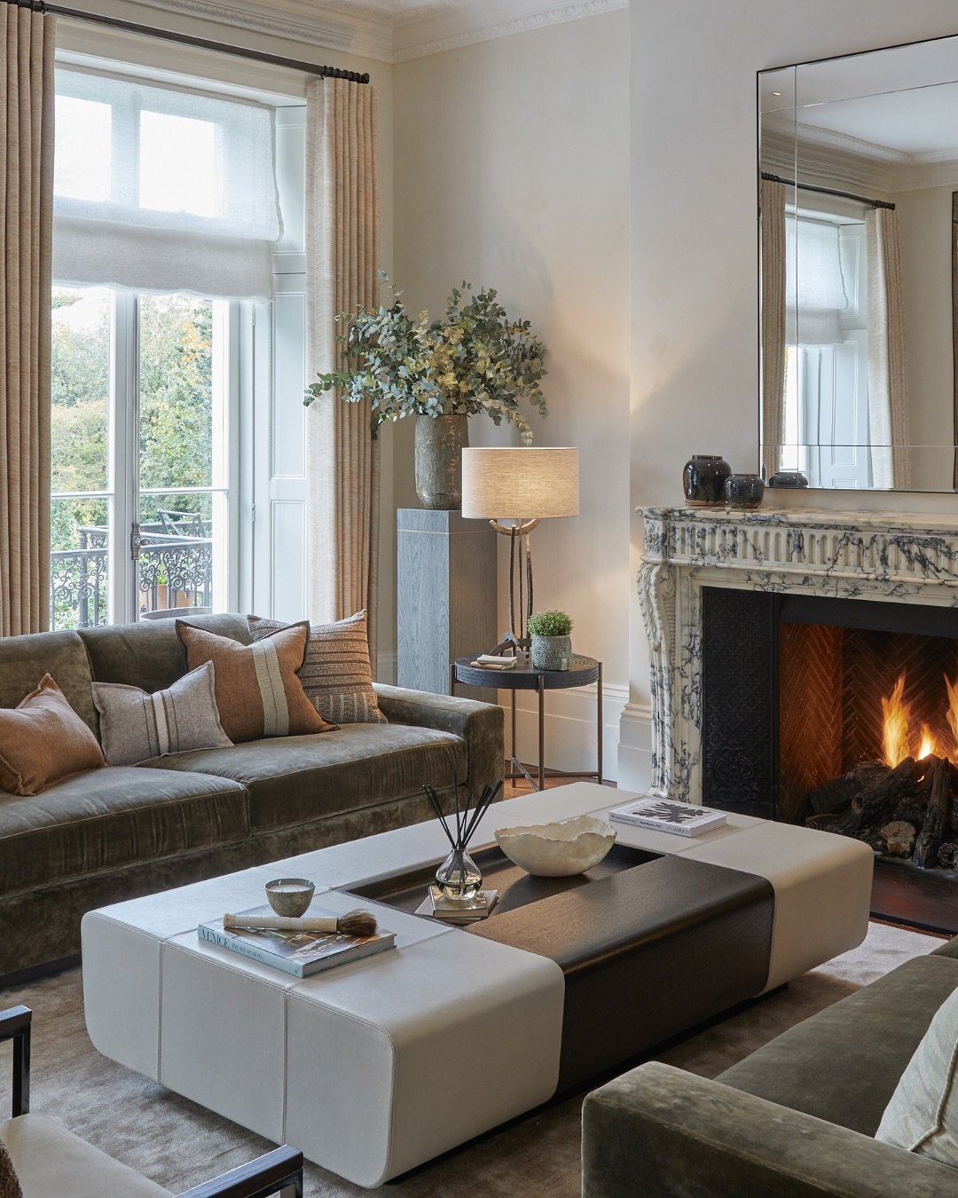 Large rectangular upholstered ottoman coffee table with dark wood tray insert near fireplace