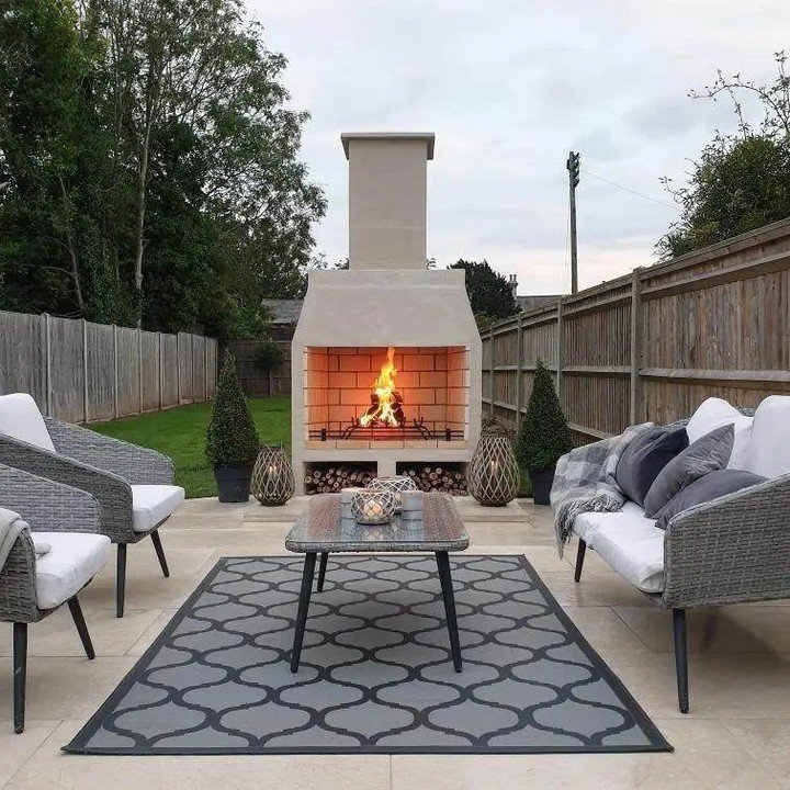 Freestanding outdoor masonry fireplace finished in smooth light stucco with a red brick firebox in a fenced backyard.