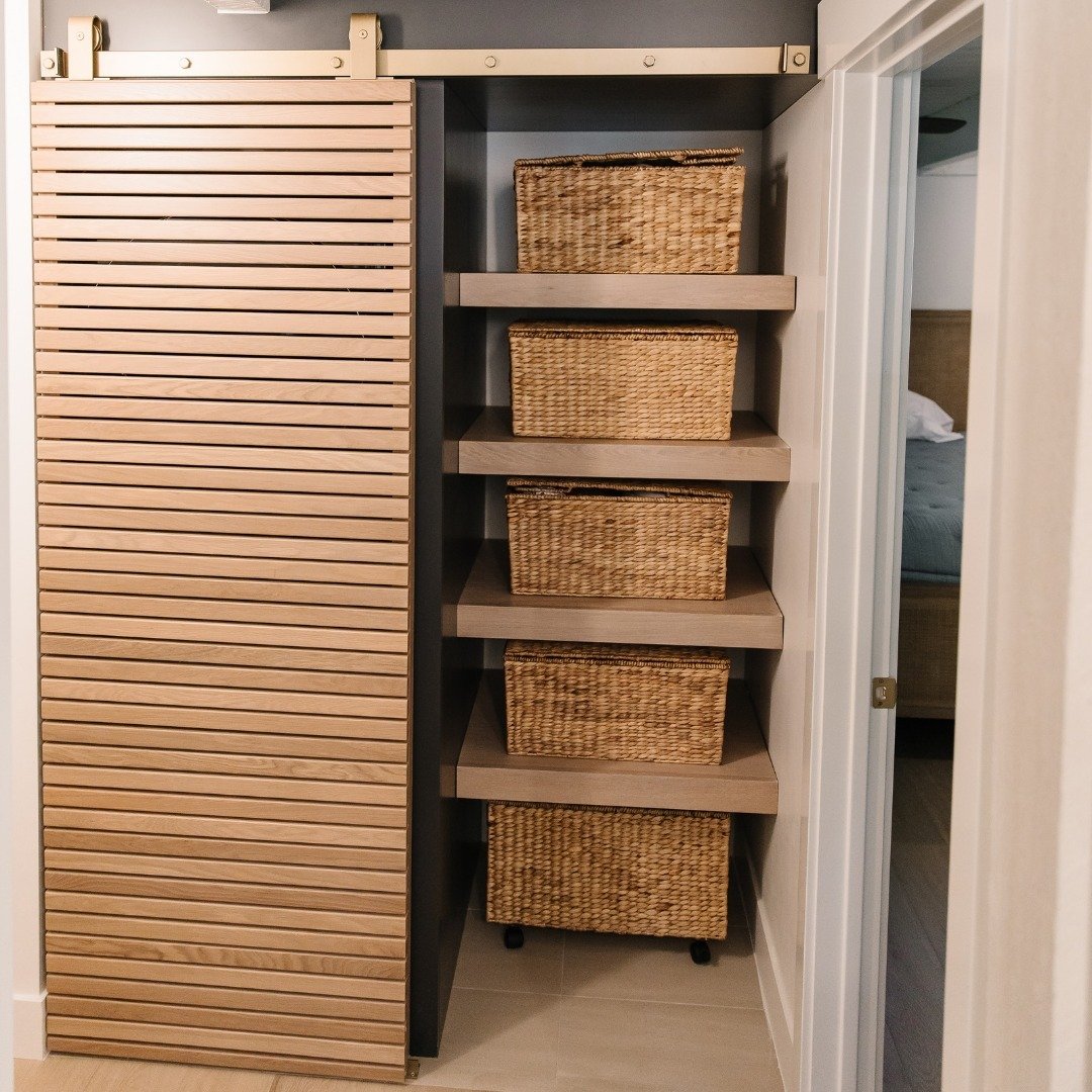 Built-in wooden laundry shelves stacked vertically behind a sliding slat door holding woven baskets