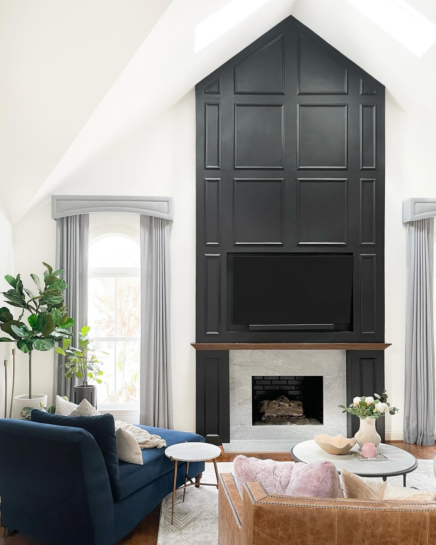 Tall, vaulted living room with a dramatic black fireplace accent wall featuring wainscoting and a marble hearth.
