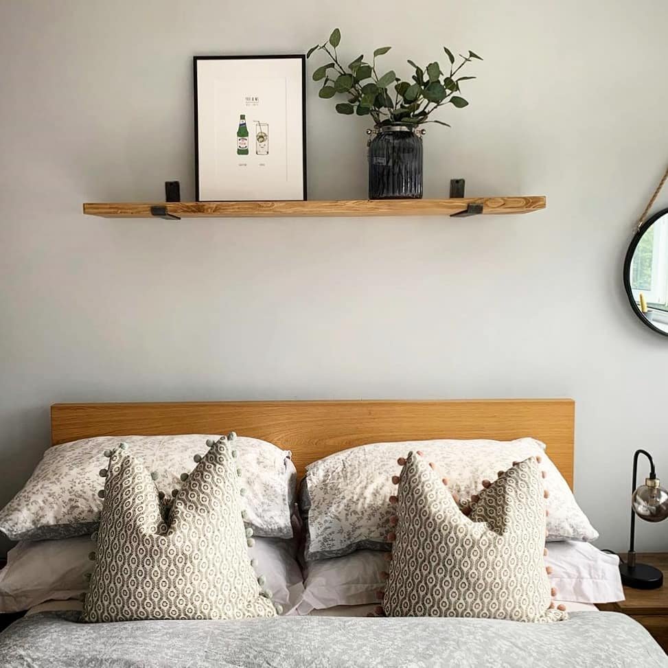 Wooden shelf above bed with black brackets holding art and vase.