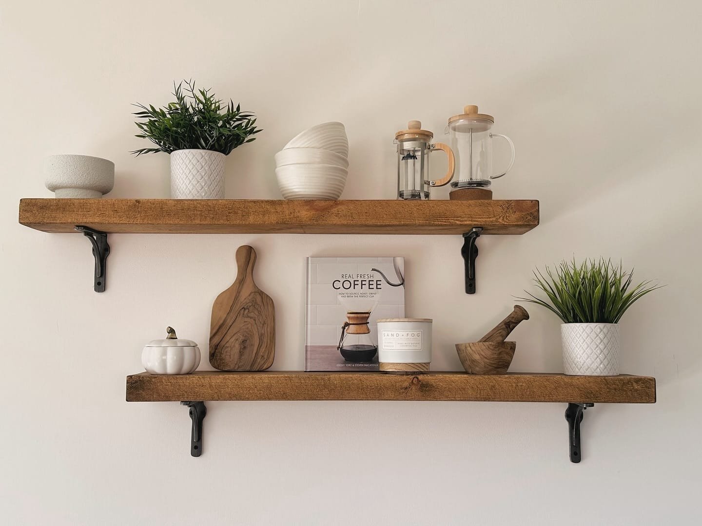 Two rustic wooden shelves held by black metal brackets, styled with coffee items and plants.