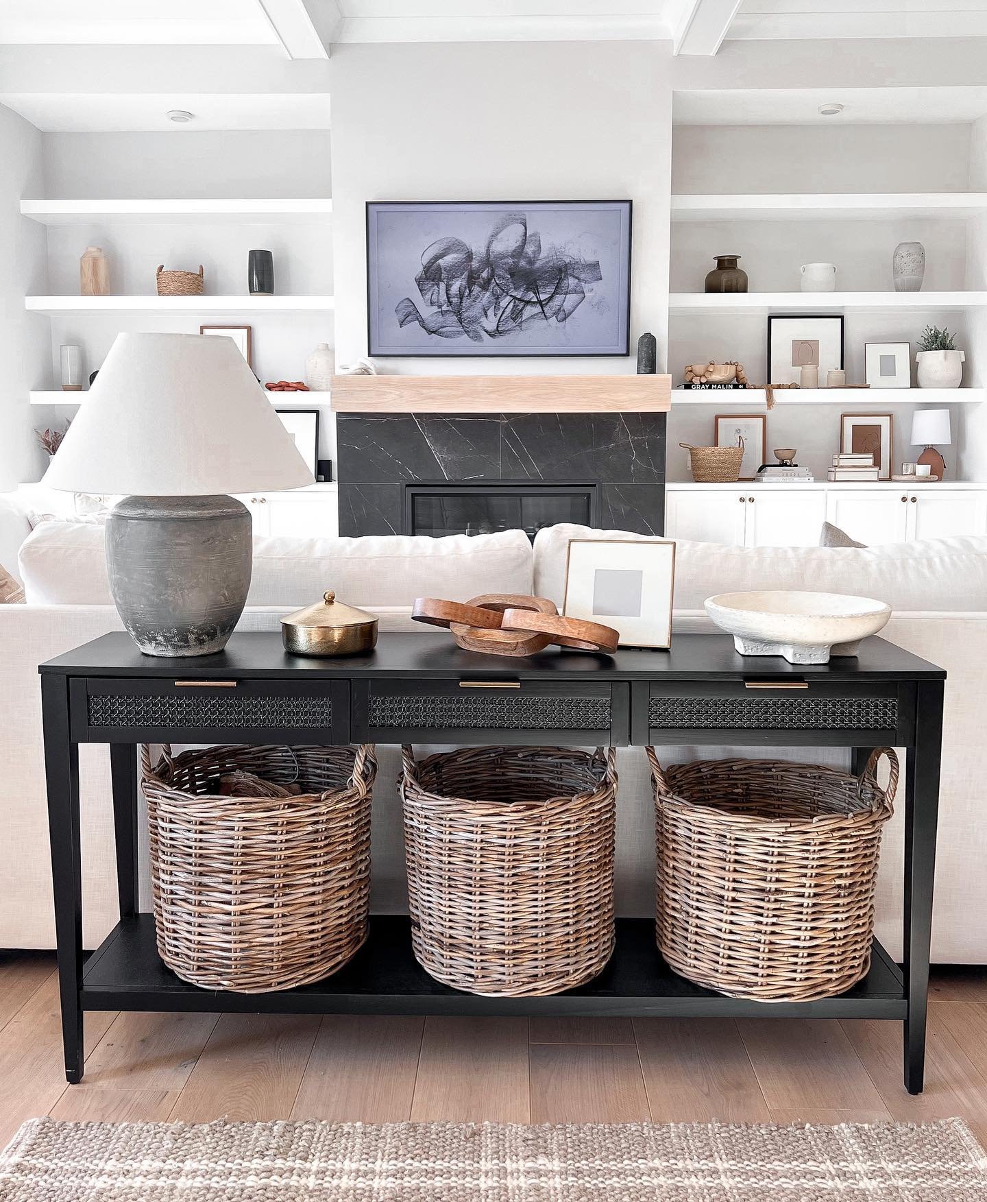 Black console table with woven drawer fronts and basket storage behind sofa