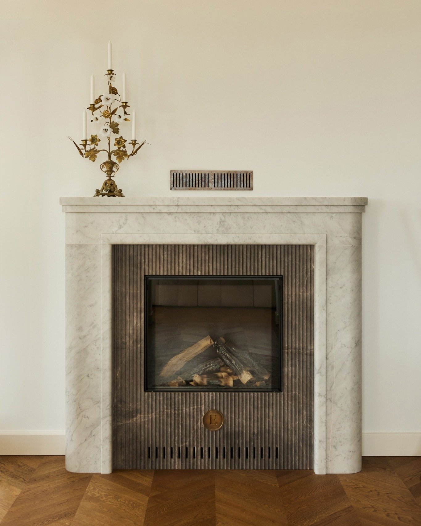An elegant fireplace featuring a curved white marble surround and a dark fluted marble insert, topped with an ornate brass candelabra.