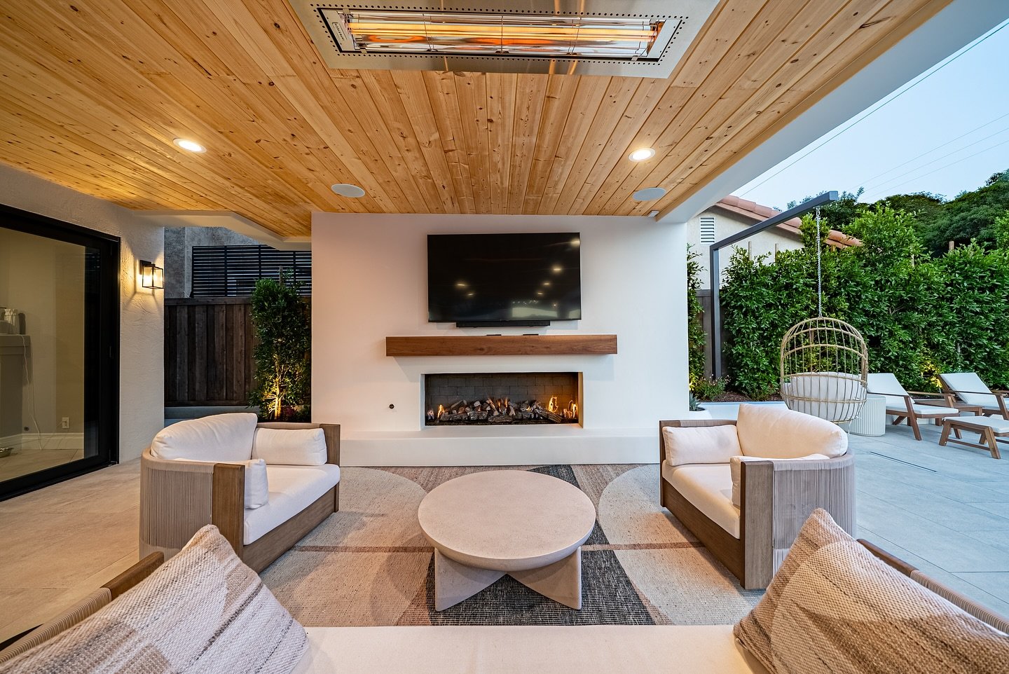 Sleek linear gas fireplace set into a white wall on a modern covered patio with a wooden ceiling.