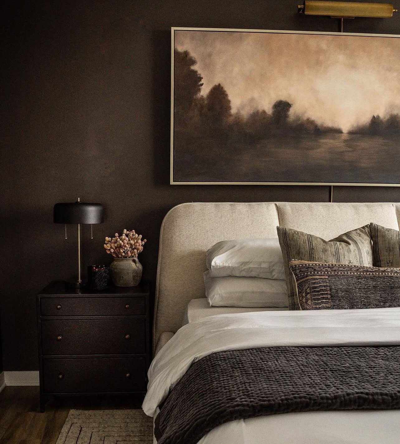 Dark brown bedroom featuring a large landscape painting above a beige upholstered headboard