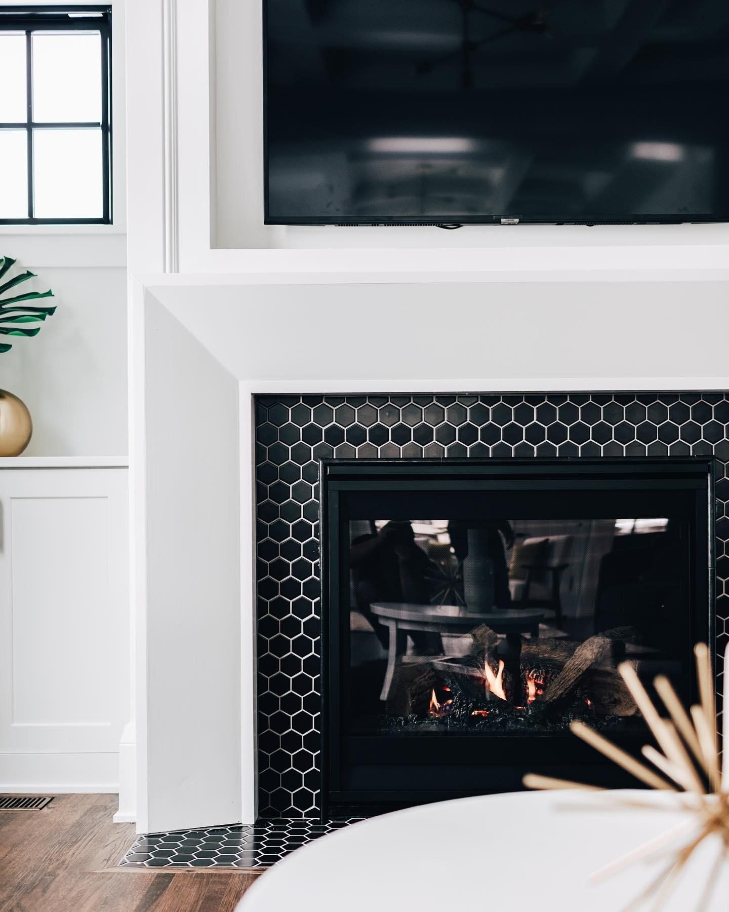 A contemporary fireplace featuring a white wood surround and an insert lined with small, black hexagon mosaic tiles.
