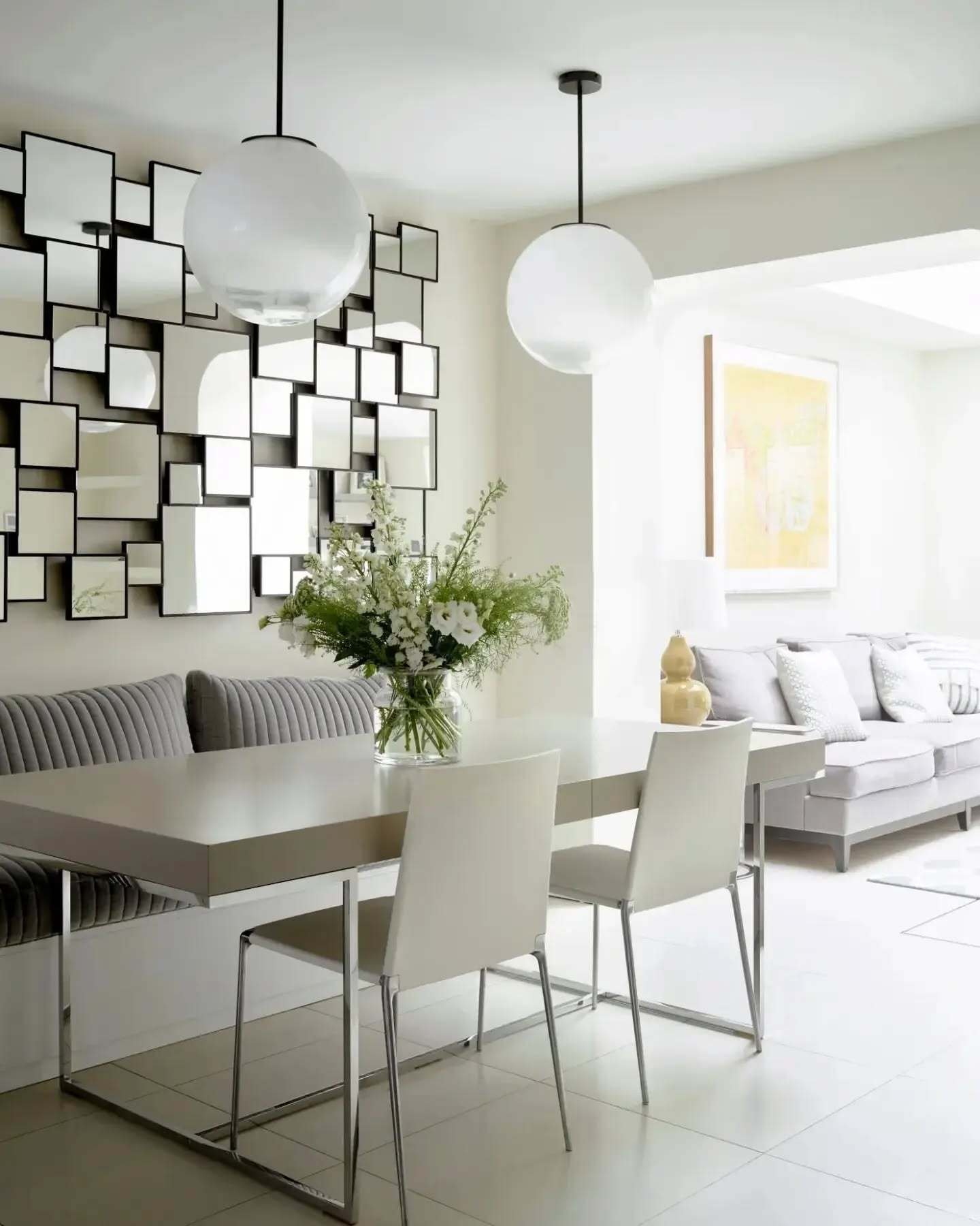 Rectangular white dining table with chrome sled legs and grey banquette