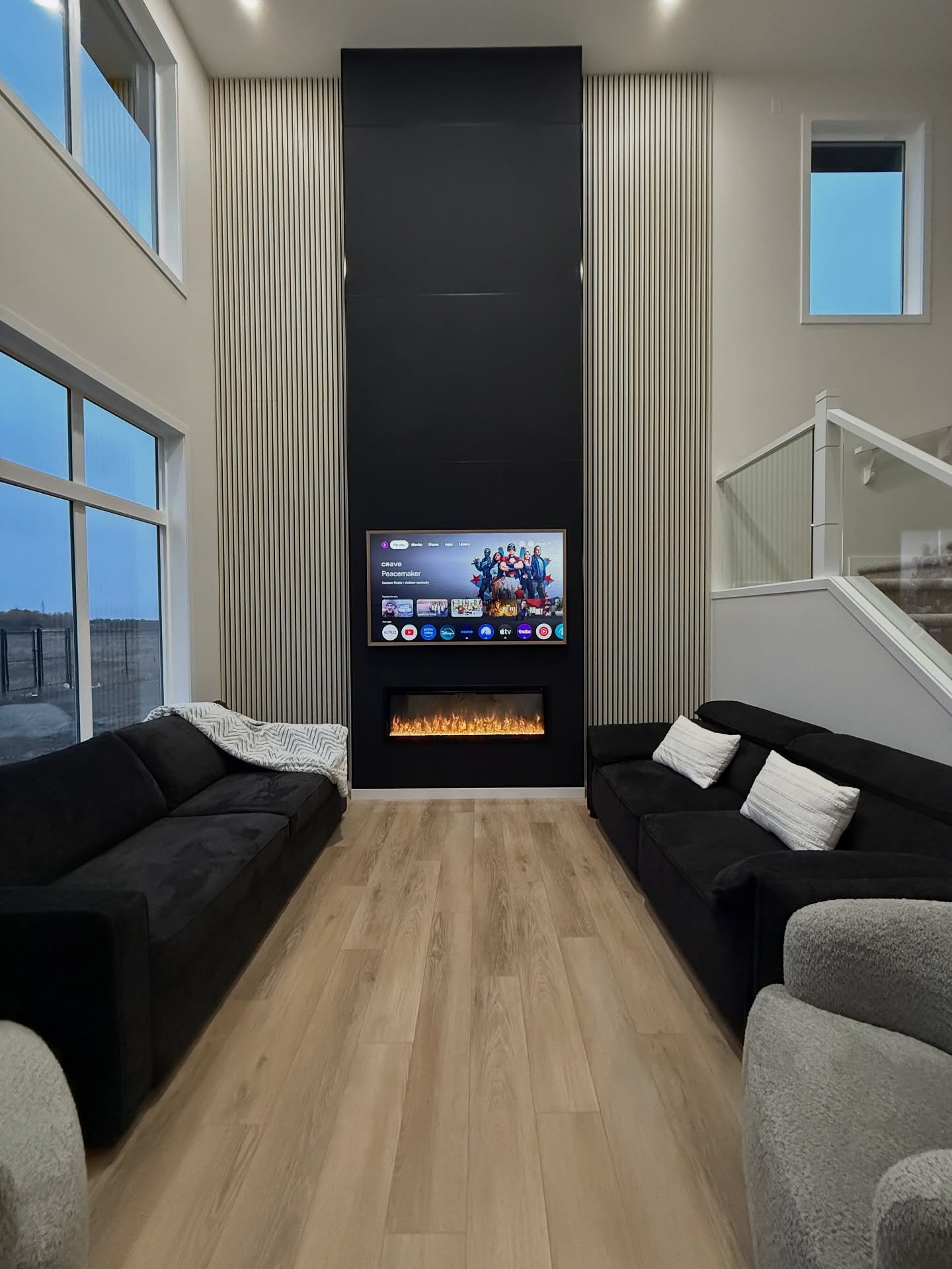 Tall, vaulted living room with a fireplace accent wall split between a central matte black panel and flanking light wood vertical slats.