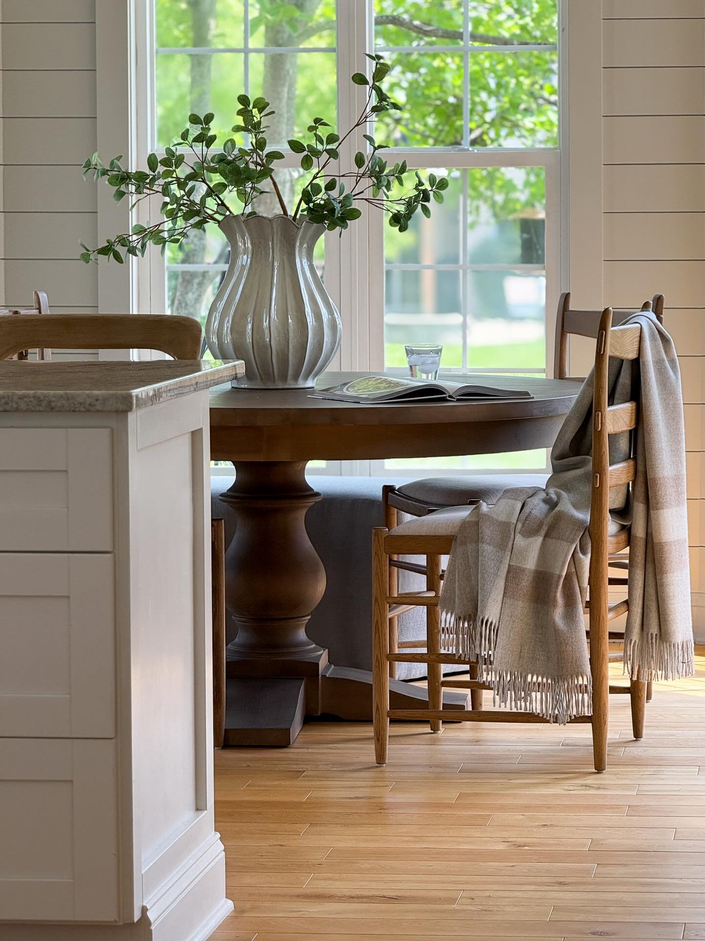Dark wood round dining table with thick pedestal base near window
