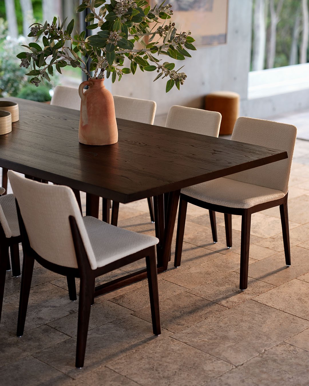 Dark wood rectangular dining table with cream upholstered chairs on stone floor
