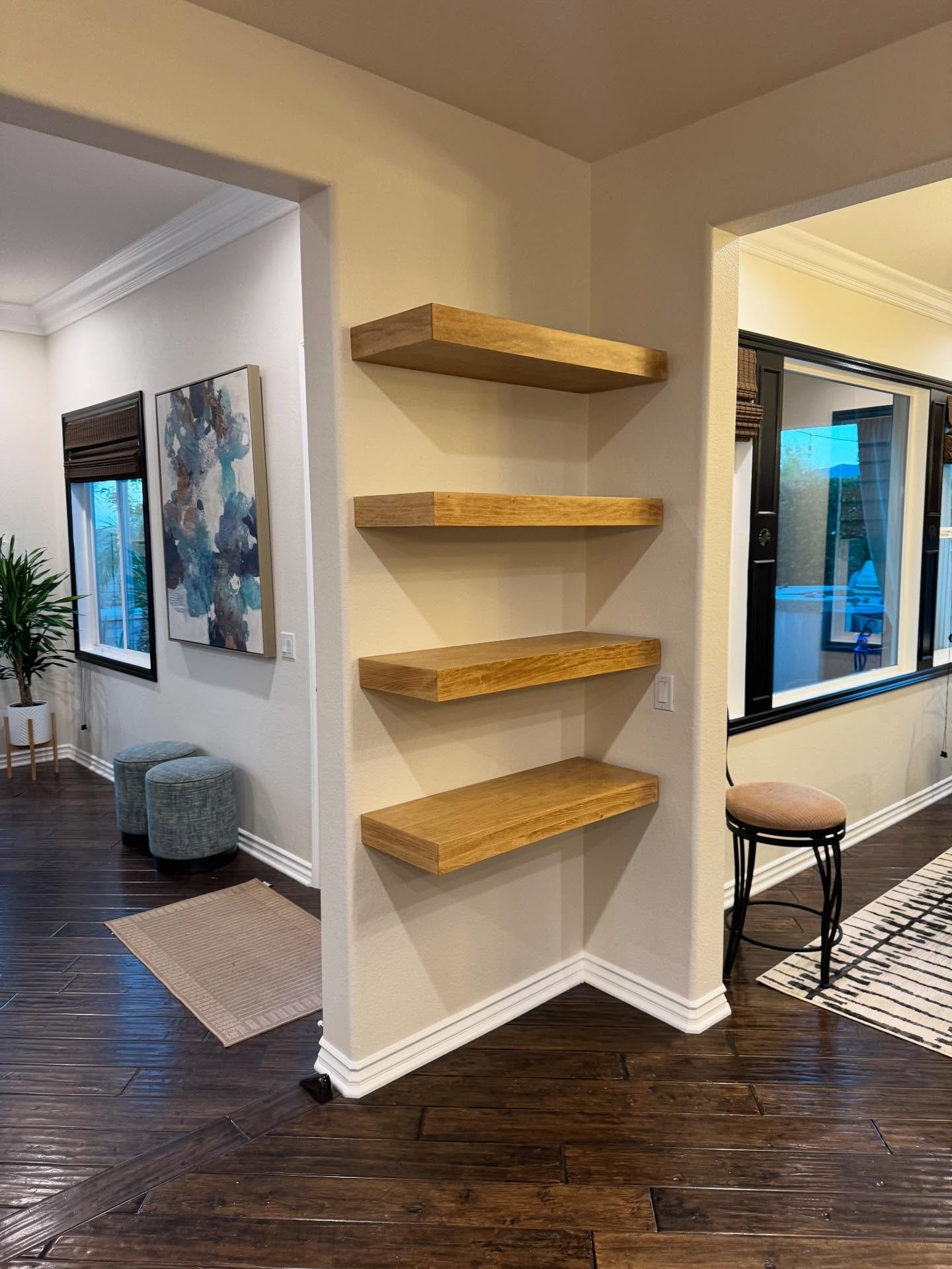 Four thick light wood floating shelves installed in a recessed angled wall alcove.
