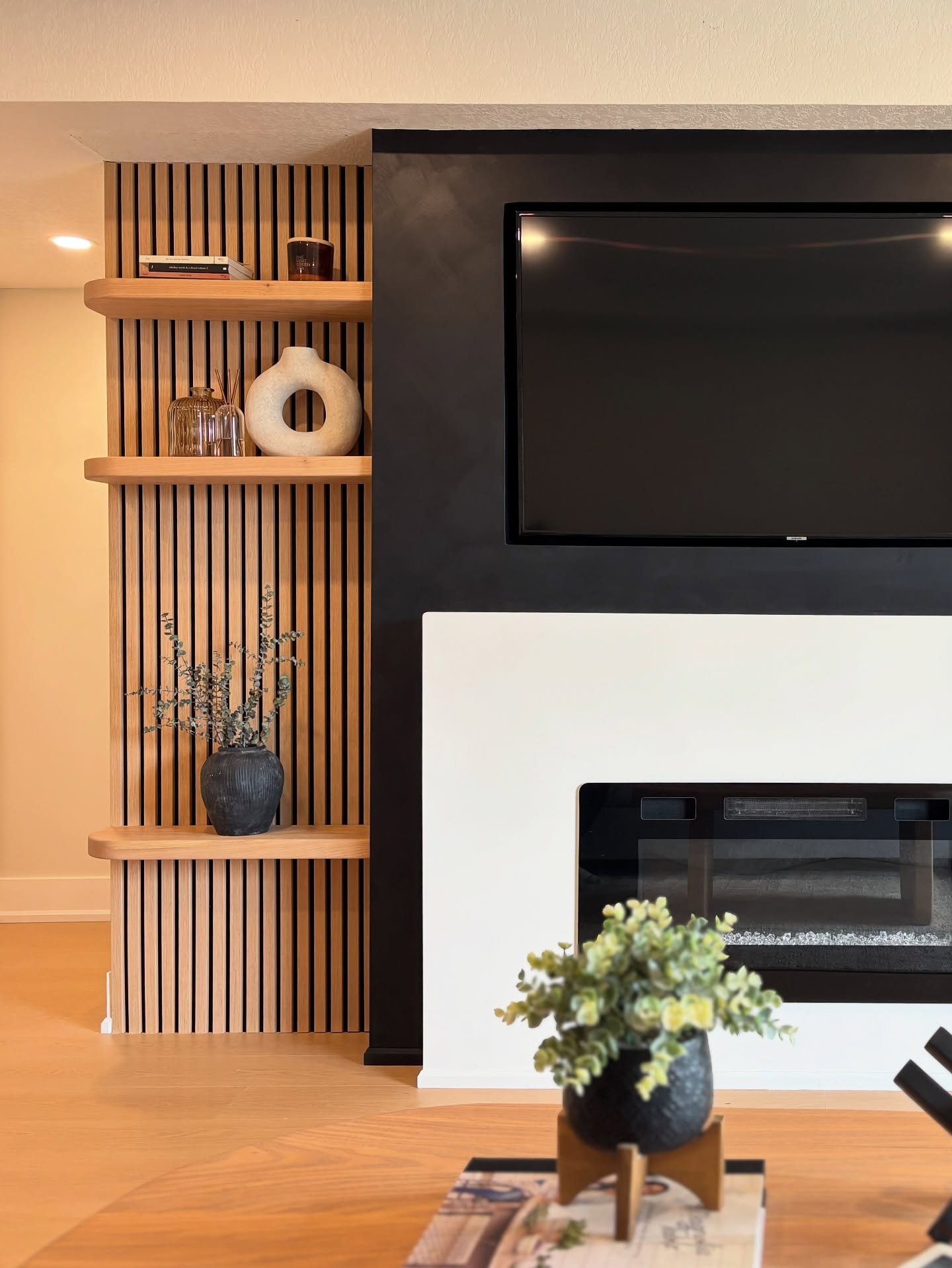 Wooden floating shelves with curved edges mounted on a vertical wood slat wall next to a modern fireplace.