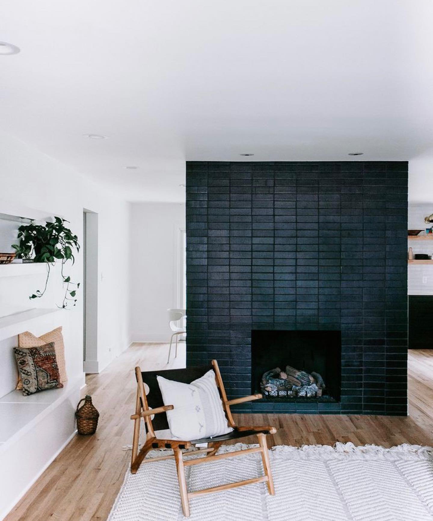 A tall, rectangular fireplace wall faced with thin, matte black brick. The dark feature wall stands against bright white walls and light wood flooring.