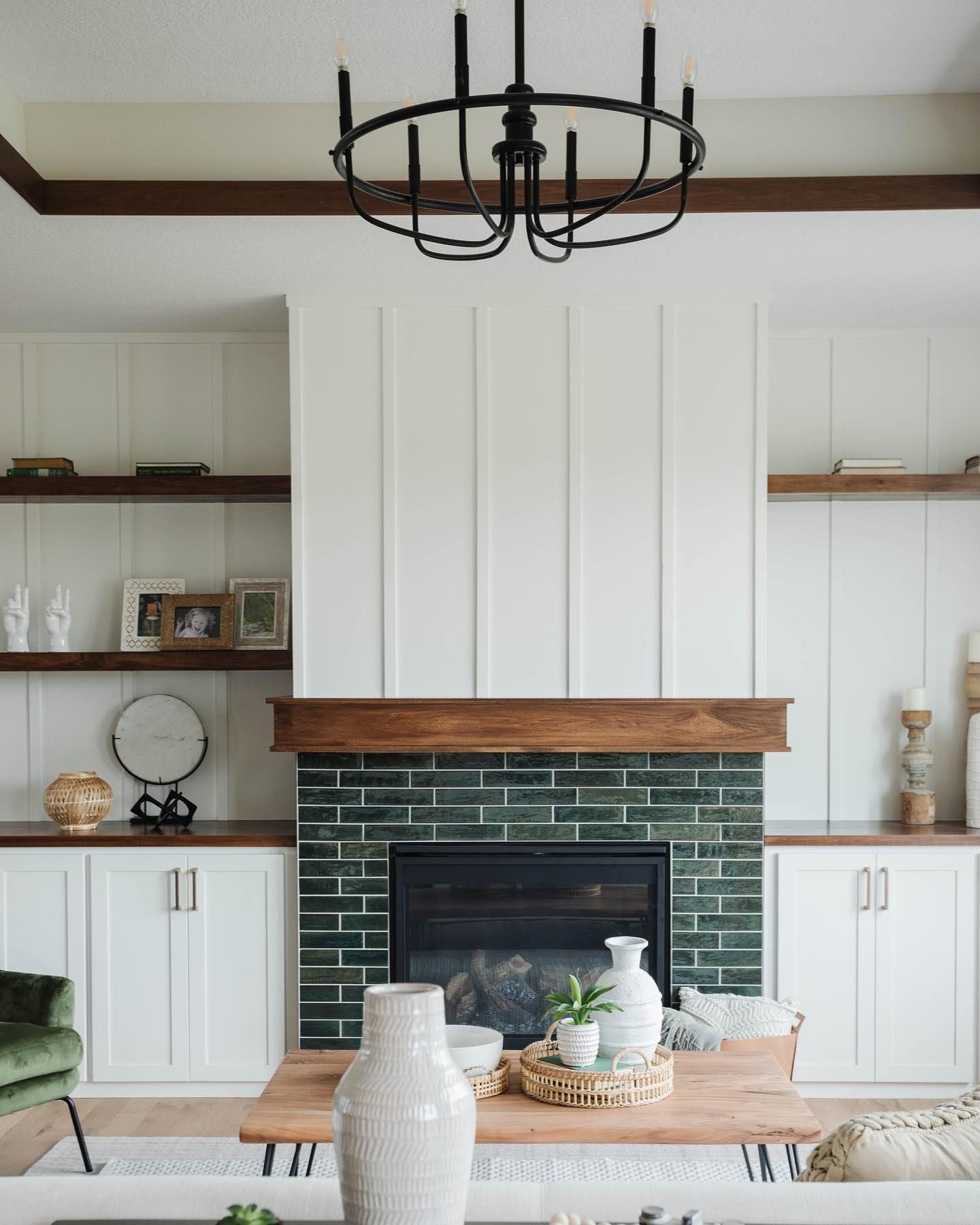 A living room fireplace with white shiplap above the mantel, featuring dark green, glossy subway tiles surrounding the firebox.