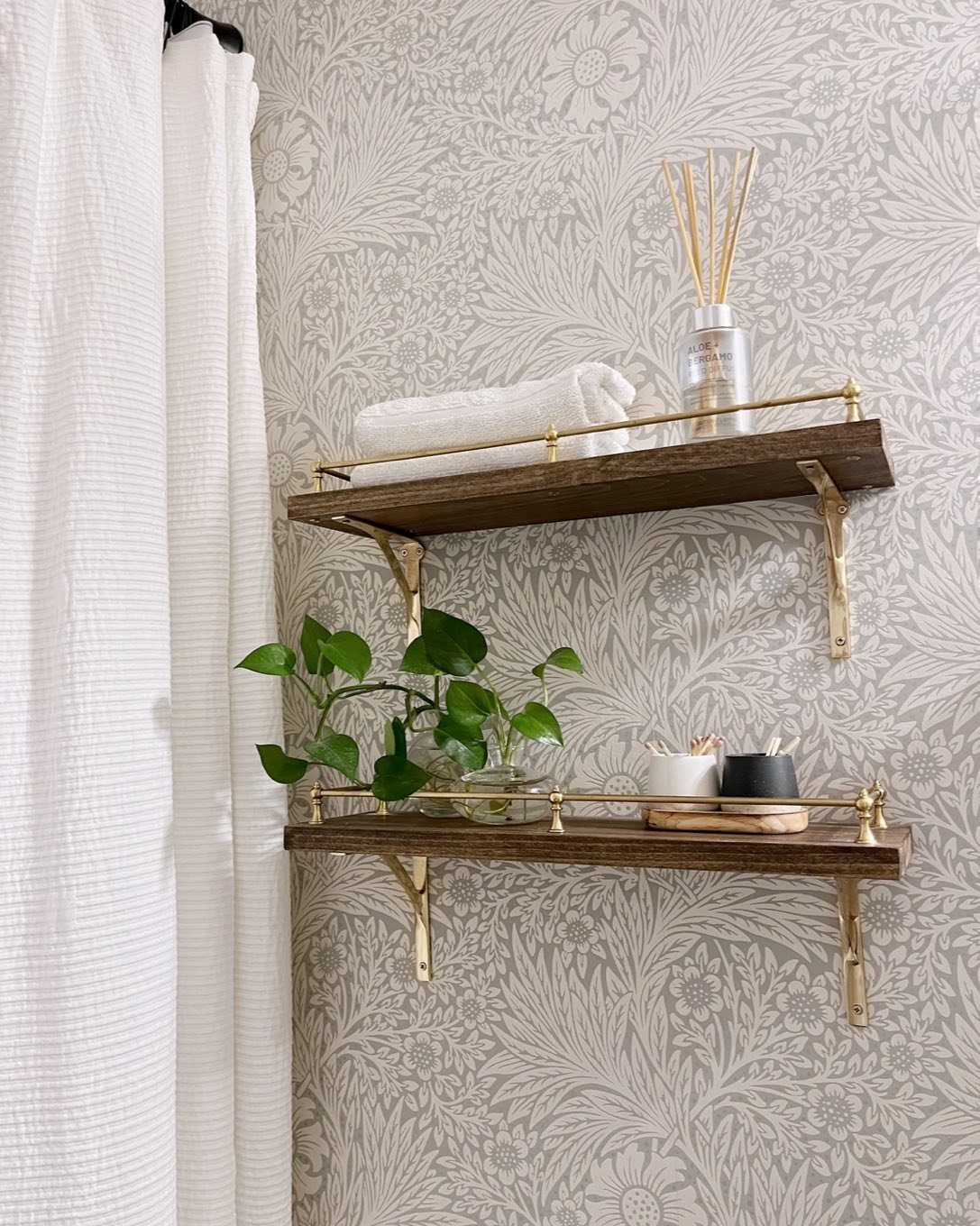 Dark wood floating shelves with gold brackets and gallery rails, mounted on floral wallpaper.
