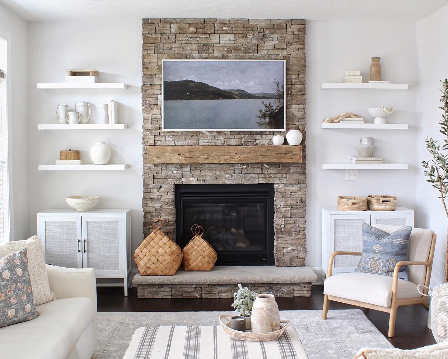 Three levels of white floating shelves flanking a stone fireplace