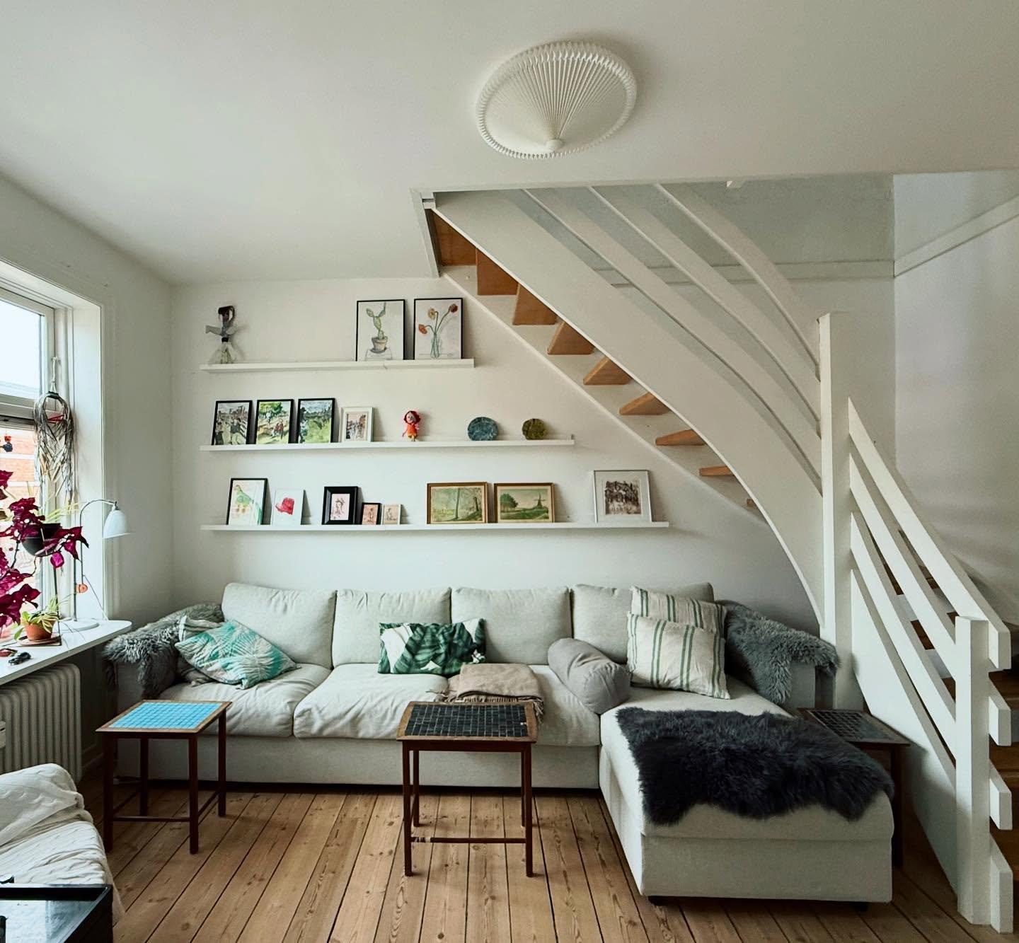 Three white picture ledges displaying small art frames on a wall under a staircase