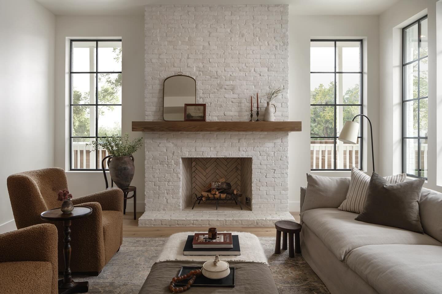 A living room featuring a floor-to-ceiling fireplace painted bright white. A natural wood mantel holds simple decor, and the firebox has a herringbone brick pattern.