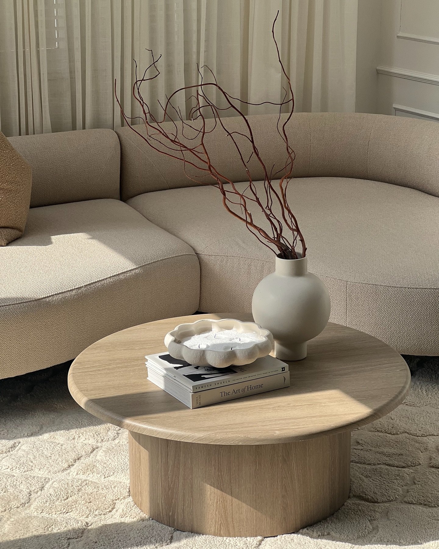 Round light oak coffee table with pedestal base in neutral living room