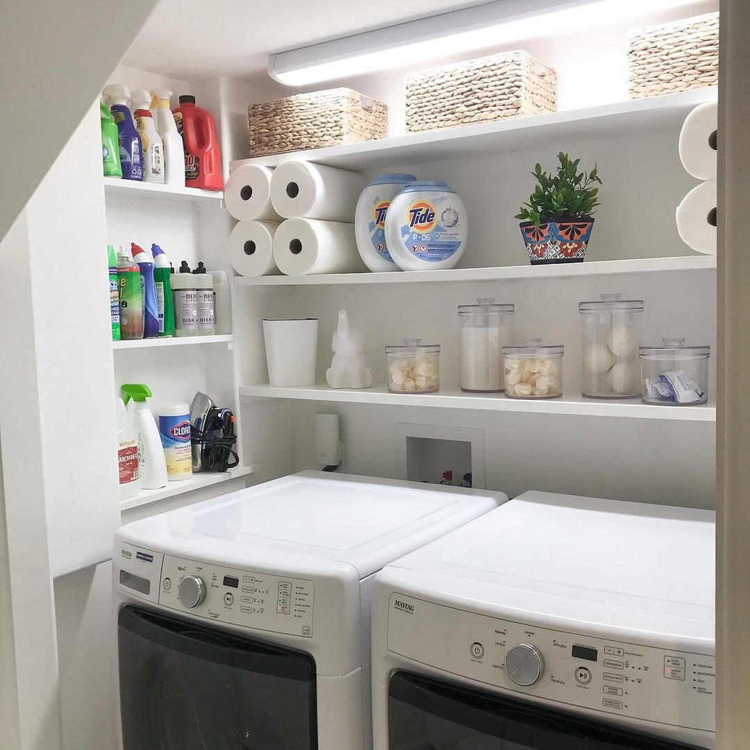 White floating laundry shelves and narrow corner ledges holding cleaning supplies above washer and dryer