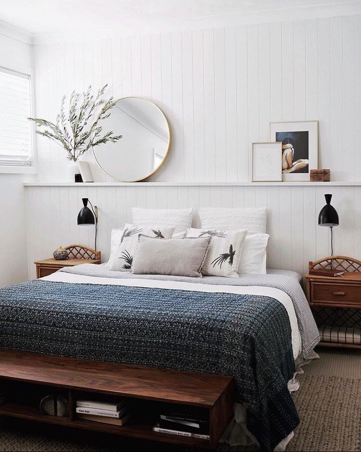 White vertical paneling wall ledge behind bed with round mirror and art.
