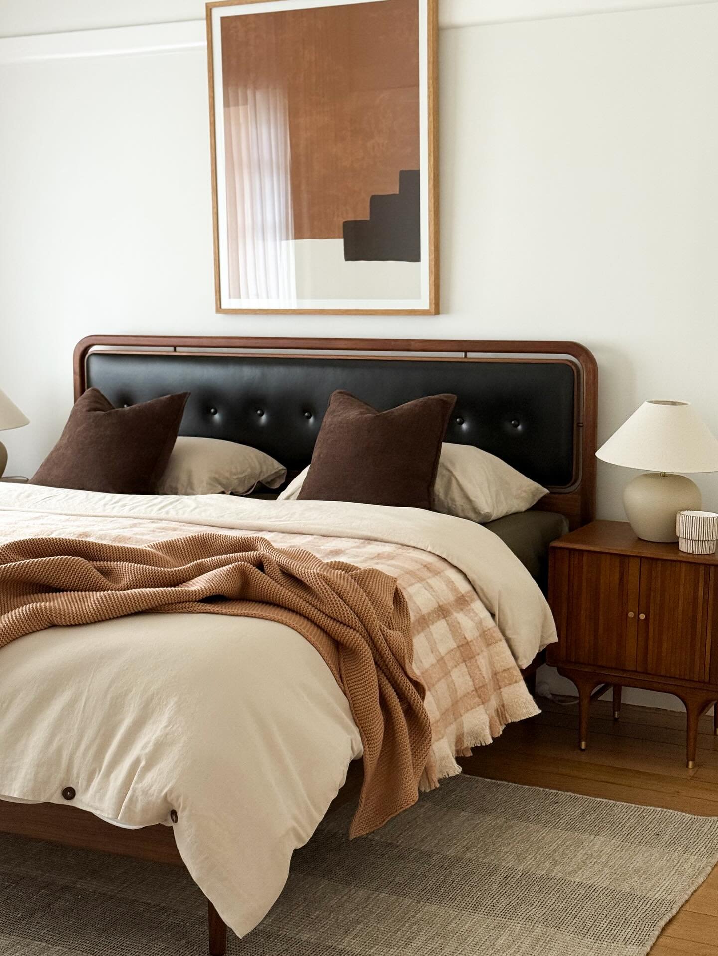 White bedroom featuring a mid-century leather headboard, wooden nightstand, and rust-colored throw blanket