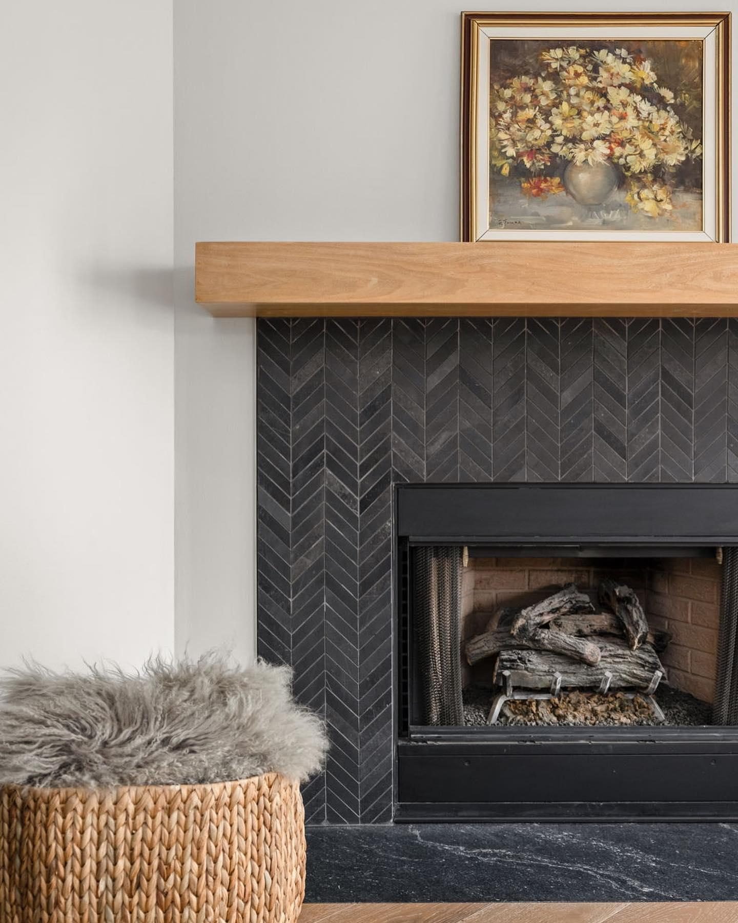 A contemporary fireplace featuring a light wood floating mantel and a surround tiled with dark charcoal slate in a chic chevron pattern.
