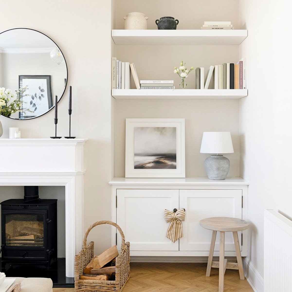White built-in alcove shelves with books and a table lamp next to a log burner fireplace.