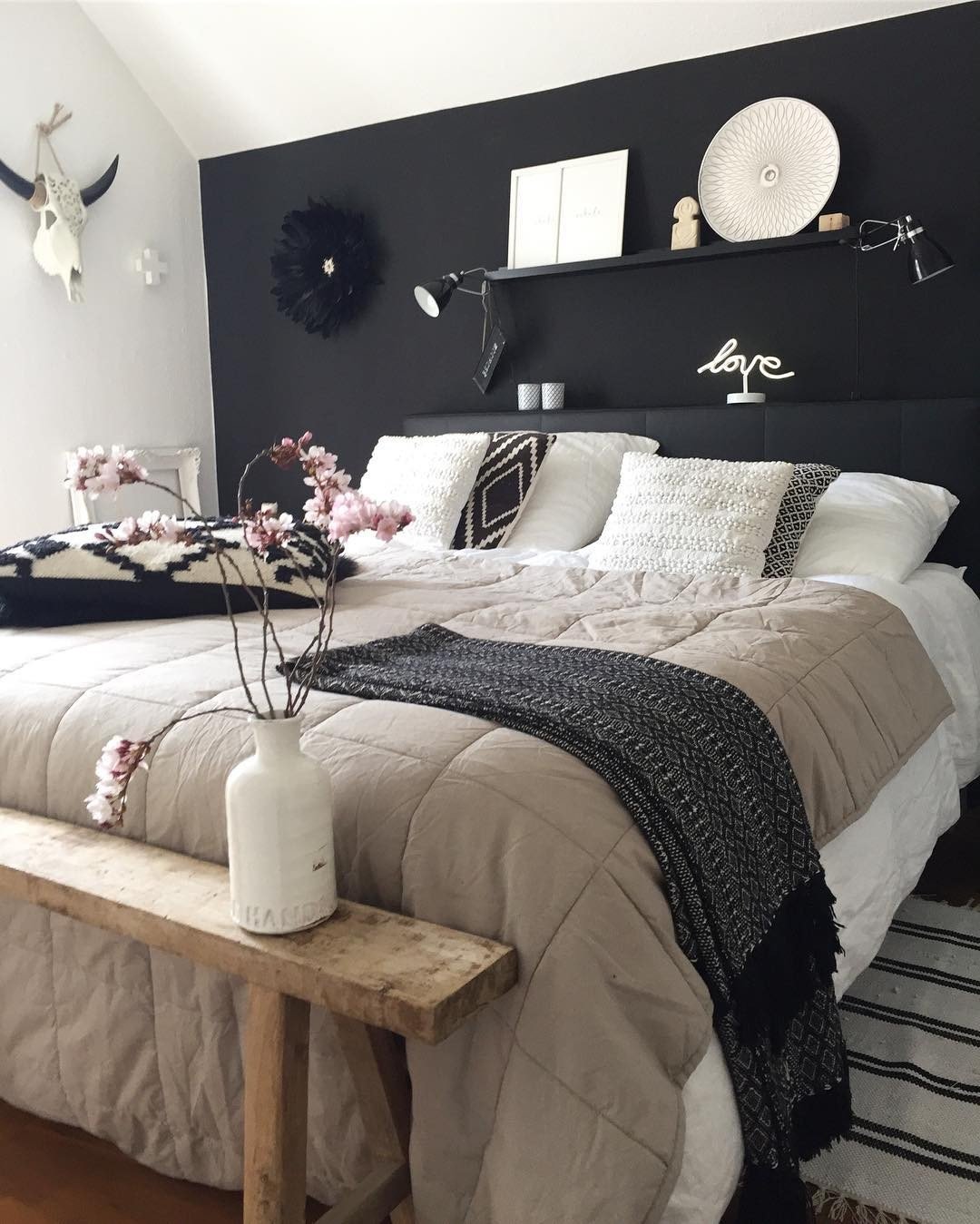 Black wall with black shelf displaying white decor above bed.