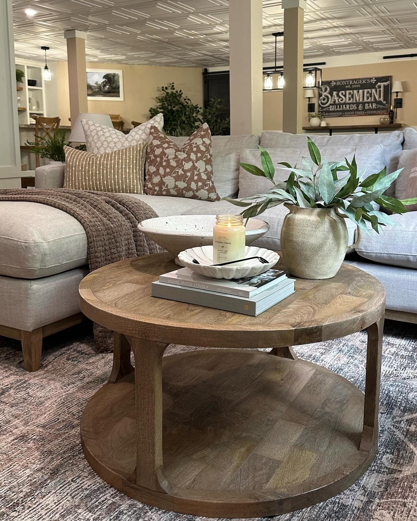 Round wood coffee table with bottom shelf and parquet top in a basement living room