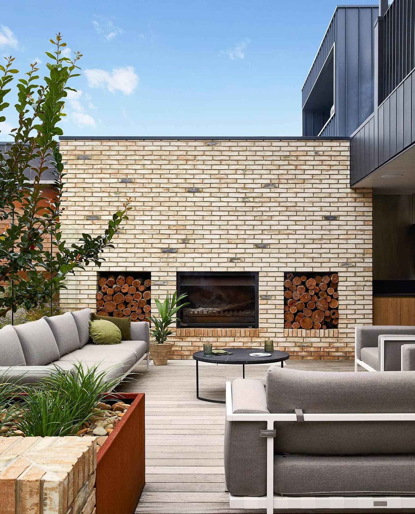 Contemporary outdoor fireplace built into a wall of yellow-toned brick with recessed log storage on either side.